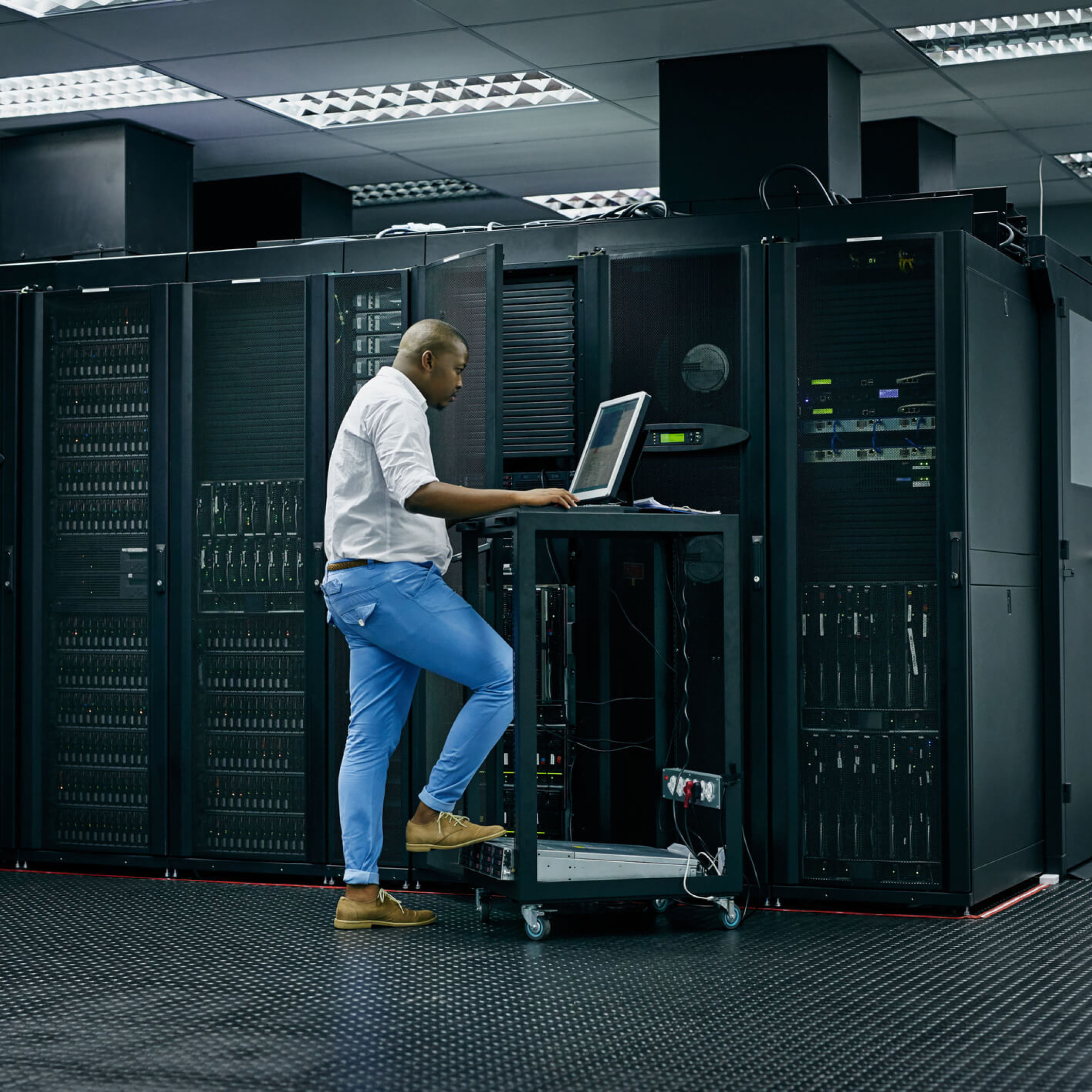 A man standing working on a computer in front of a server